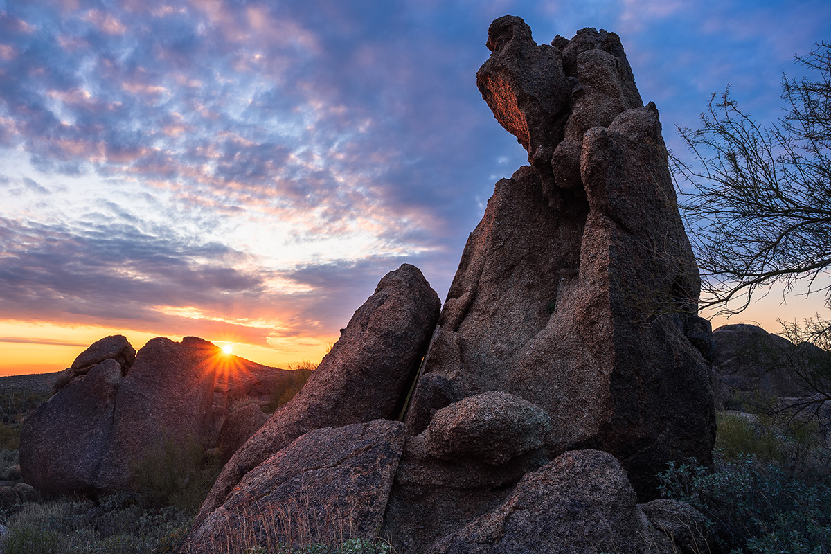 Sun cresting over boulders in the distance. While a spire of stone looms over you.